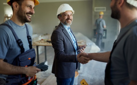 Image of 3 men at a work site in hard hats, 2 are shaking hands