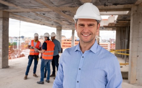 Image of a smiling man in a hard hat at a high-rise building site